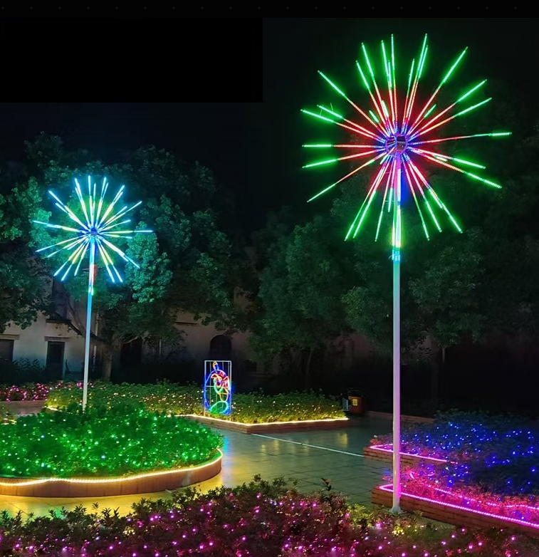 Color-changing RGB fireworks lights on tall poles in a landscaped garden courtyard, surrounded by LED ground lighting and floral installations