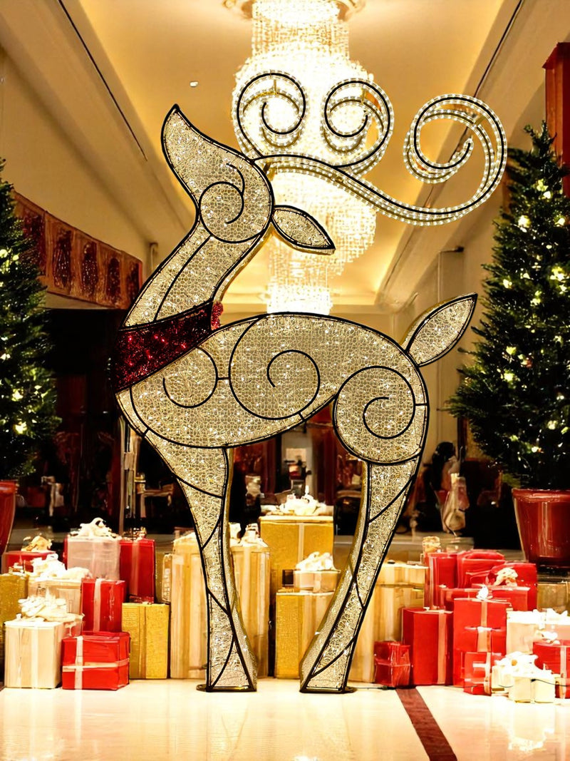 Tall gold LED reindeer sculpture with swirling light design and red scarf, surrounded by wrapped gifts and Christmas trees in a grand holiday lobby