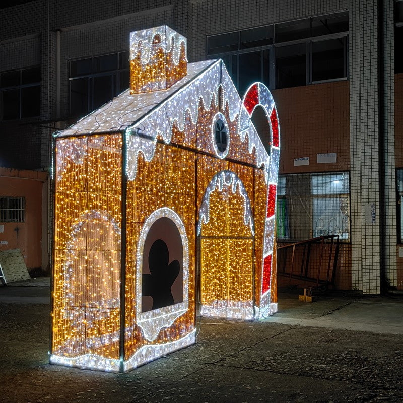 Side view of illuminated gingerbread house holiday display featuring warm white LED lights, candy cane accent, chimney, and gingerbread cutout window