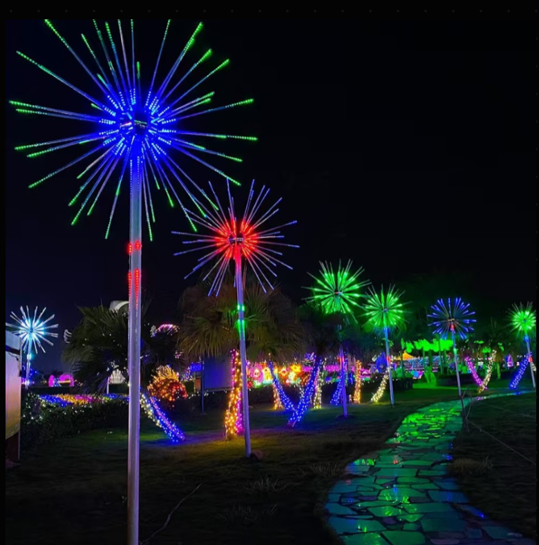 Pole-mounted RGB DMX fireworks lights in blue, red, and green illuminating a landscaped path lined with palm trees and wrapped trunks in a nighttime setting